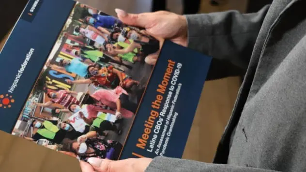 HF Director of Grants holding a report Hispanic Federation issued mid 2024.
